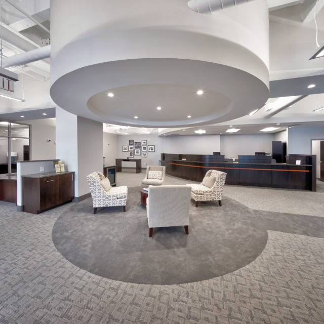 Textured gray carpet is sectioned off with custom circular solid gray in waiting area